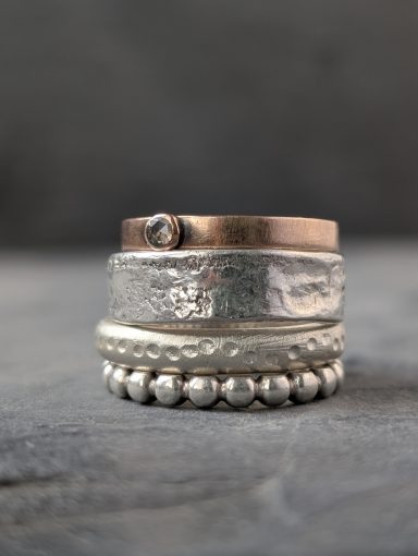 Stapelringe aus Silber und Rotgold mit verschiedenen Texturen liegen übereinander