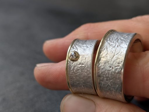 2 Eheringe mit Goldrand und Diamant werden zwischen zwei Fingern gehalten