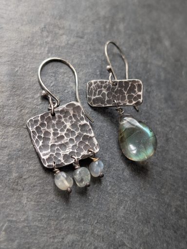 2 unterschiedliche asymmetrische Ohrringe mit geschmiedeter oxidierter Textur und Labradorit liegen nebeneinander